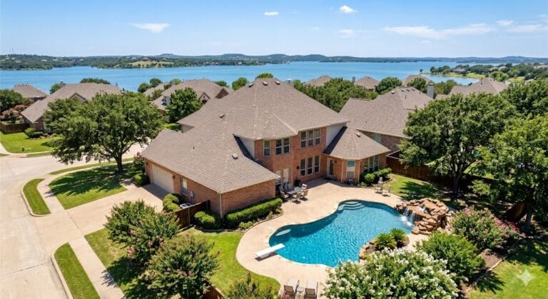 Aerial view of a luxury beautiful brick corner home in USA featuring a large backyard with a custom diving pool, rock waterfall, and a scenic lake in the background. Some like this are in Texas, California, Florida and other parts of the US as well. USA Houses buy homes new houses sell houses gateway, The American Dream. Beautiful luxury homes, USA houses for sale, new construction, and real estate investment opportunities.
