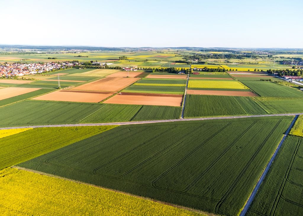 Land. USA Land. Stunning aerial view of vibrant patchwork agricultural fields and a distant village. Buying land, selling land, owning land, buy land and sell land on USAHouses.com