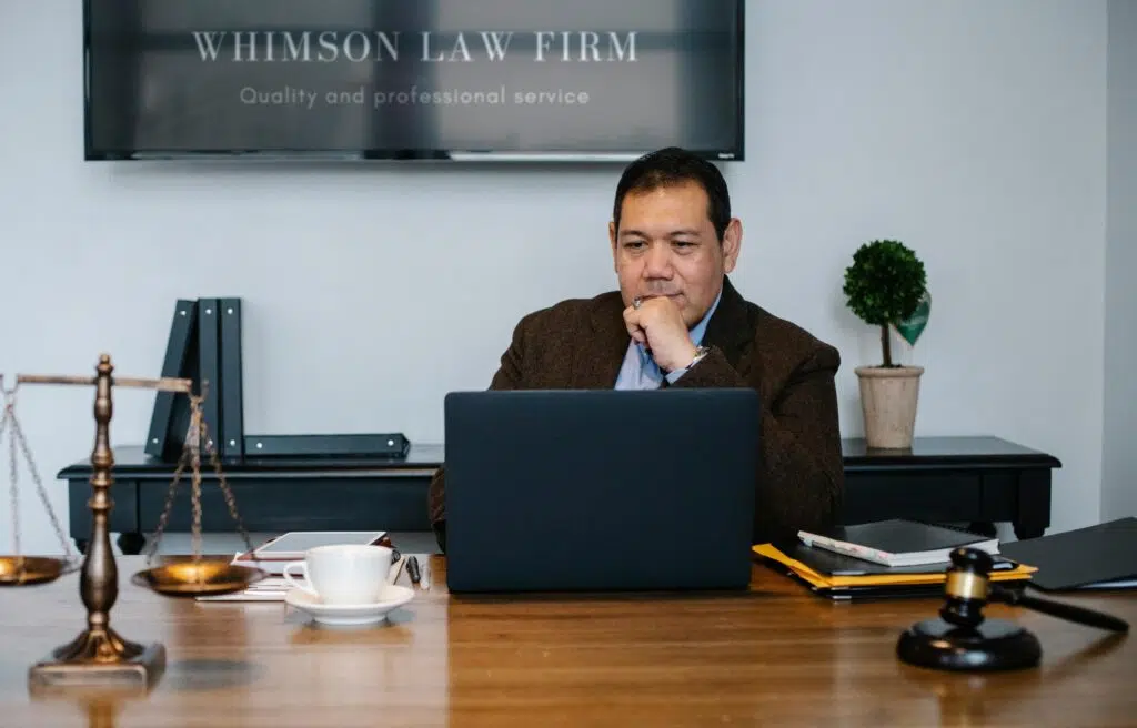Serious ethnic mature man in formal outfit working with netbook at table with gavel, privacy policy, terms of use, industry partners
