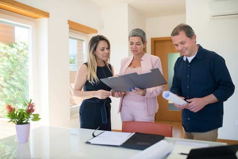 Real Estate Insights. Three real estate professionals examining documents in a modern office setting, focusing on a property sale. Careers, Partners, Buyers, Sellers, Investors.